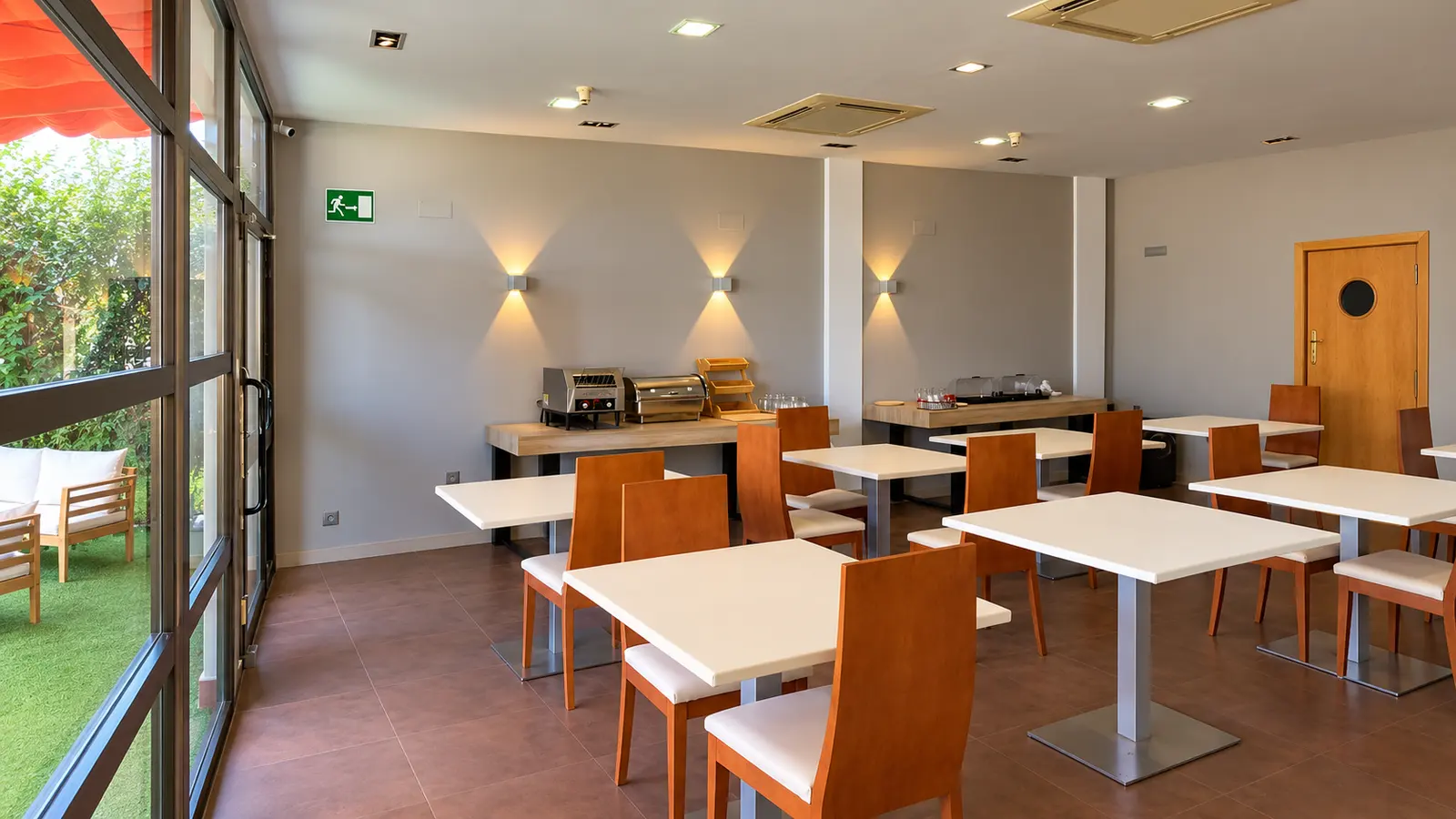 Hotel dining room with white tables, wooden chairs and large windows onto the terrace