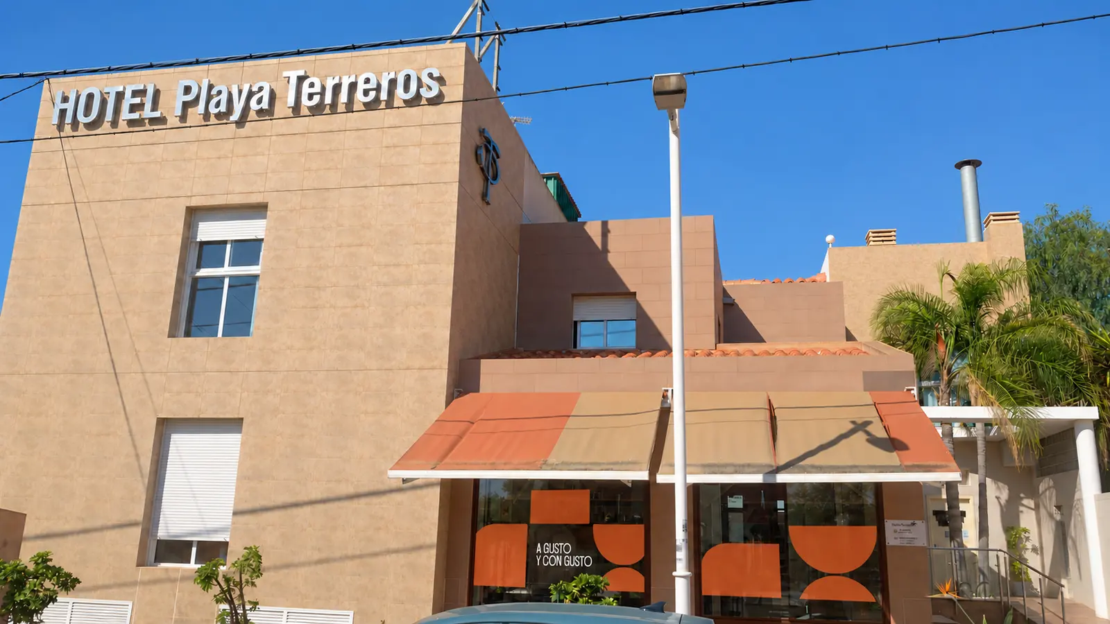 Fachada del Hotel Playa Terreros con el rótulo, el toldo naranja y las palmeras